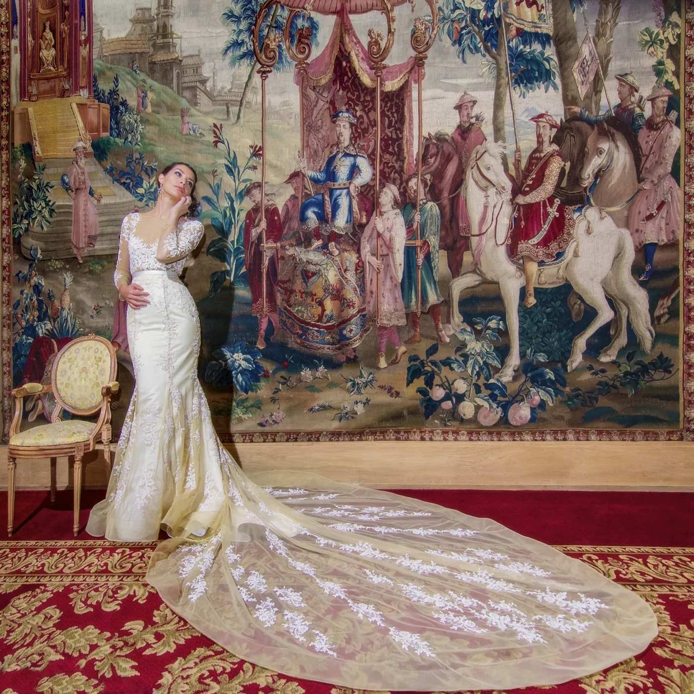 Euterpe. A bride in a lace couture gown with a sweeping train, in front of a tapestry.